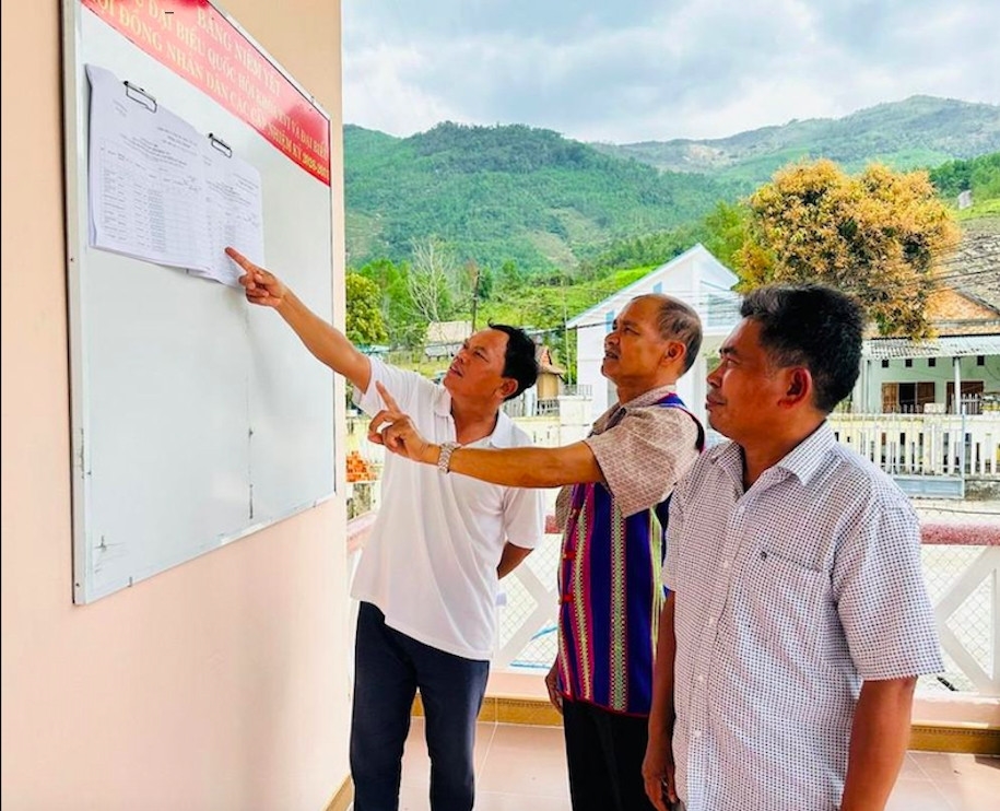 Ông Trần Văn Lũ (ở giữa) tuyên truyền giúp người dân nắm rõ thông tin tiểu sử, quá trình công tác của các ứng cử viên đại biểu Quốc hội và đại biểu HĐND các cấp. (Ảnh: D.Đ)