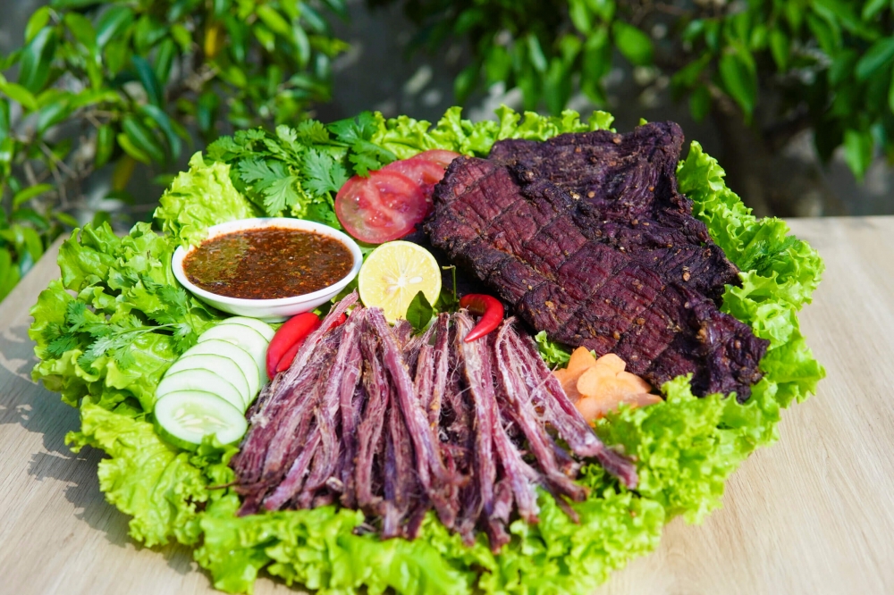 Thịt trâu gác bếp là đặc sản nổi tiếng của vùng núi Sơn La, đặc biệt được đồng bào Thái và Mông ưa chuộng. Thịt trâu tươi, thường là phần bắp, được thái dọc thớ, ướp với mắc khén, hạt dổi, ớt, gừng và nhiều gia vị núi rừng, rồi treo lên gác bếp hun khói từ củi thơm. Nhờ cách làm này, thịt vừa khô, vừa thấm đậm gia vị, lại giữ được vị ngọt đặc trưng. Khi ăn, chỉ cần nướng lại hoặc hấp cho mềm, xé từng sợi chấm với chẩm chéo là đã cảm nhận trọn hương vị cay, thơm, mặn mà của núi rừng Tây Bắc.