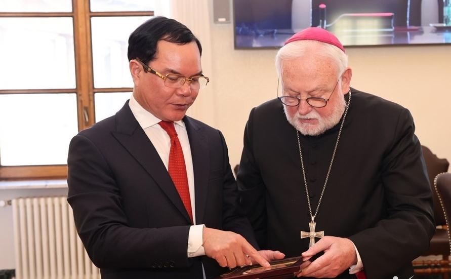 Bộ trưởng Nguyễn Đình Khang giới thiệu với Bộ trưởng Bộ Ngoại giao Tòa thánh Vatican - Tổng Giám mục Paul Richard Gallagher ý nghĩa quà tặng lưu niệm được Đoàn công tác Bộ Dân tộc và Tôn giáo Việt Nam tặng Giáo hoàng.
